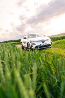 White car surrounded by vegetation and fields under a partly cloudy sky, Deer E- CarSharing,