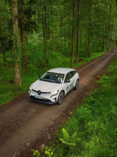 A car drives along a quiet forest path surrounded by dense green forest, Deer E- CarSharing,