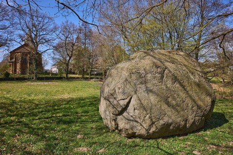 Boulder from southern Sweden, granite, Saale Ice Age, lawn, bare winter trees, blue cloudless sky,