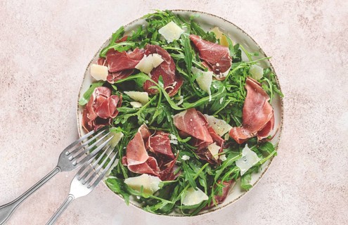 Fresh arugula salad with prosciutto and grated parmesan cheese, on a plate, homemade, no people