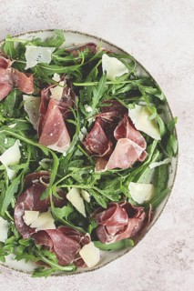 Fresh arugula salad with prosciutto and grated parmesan cheese, on a plate, homemade, no people