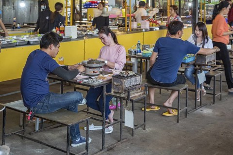 Thai couple cooking on a hot pot and eating at a buffet style outdoor restaurant in Chiang Rai