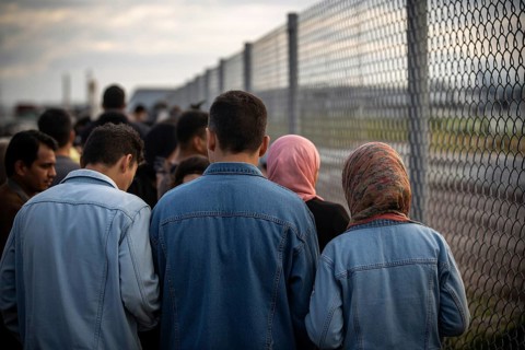 Immigrants at border crossing facing uncertain future. Men in denim and women in hijabs stand