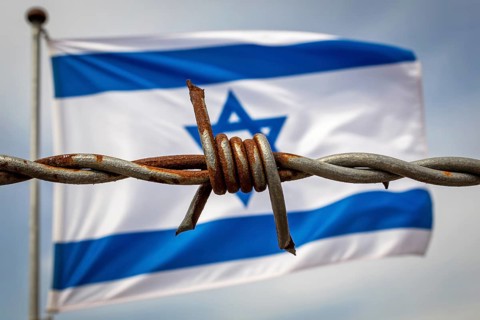 Rusty barbed wire in sharp focus with waving Israeli flag in blurred background. Symbol of