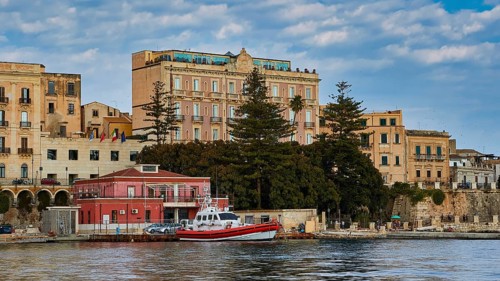 Boats in front of historic buildings and trees on a ponderous coast under a cloudy sky, boat trip