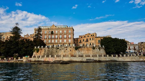 Large historic facades with manicured trees on an elevated coastline, boat trip around the island