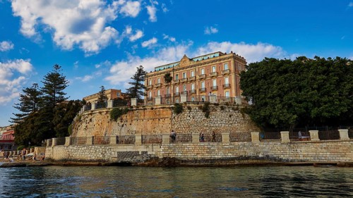 Magnificent building on a cliff, surrounded by lush vegetation and clear skies, boat trip around