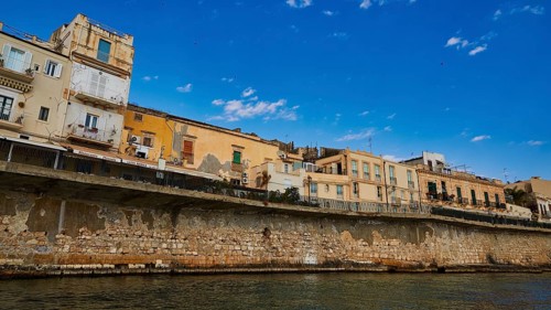 Row of historic houses on a stone seawall under a clear sky, boat trip around the island of