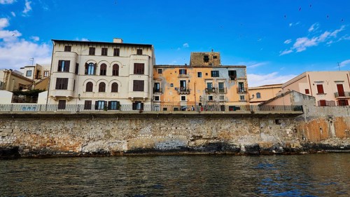 Historic buildings along a stone seawall under an expansive blue sky, boat trip around the island
