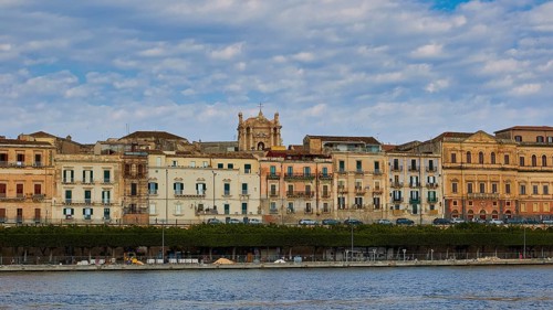 Rows of historic buildings along a coastal promenade under a patterned sky, boat trip around the