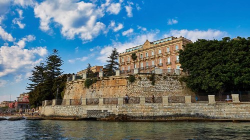 Impressive building on a cliff with lush trees and sunny sky, boat trip around the island of
