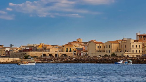 Town by the sea with old buildings and small boats, blue sky above, boat trip around the island of