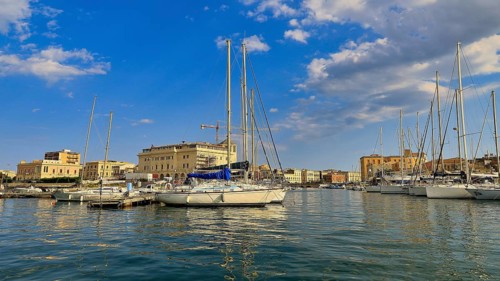 Several sailing boats moored in a marina, surrounded by a sunny city view, boat trip around the