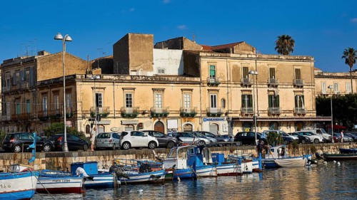 Fishing boats in a harbour in front of historic buildings and parked cars, boat trip around the