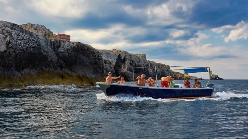Group of people on a boat near rocky cliffs, boat trip around the island of Ortigia, Isola di