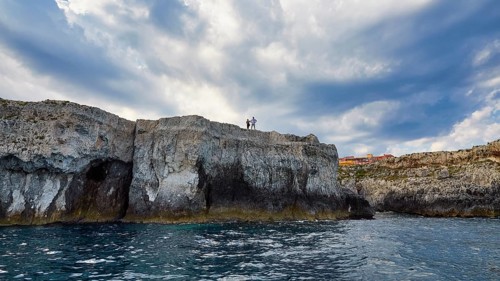 People standing on cliffs under a dramatic sky by the sea, boat trip around the island of Ortigia,