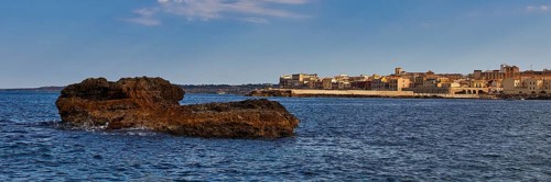Coastal cliffs in the foreground with a town and blue sky in the background, boat trip around the