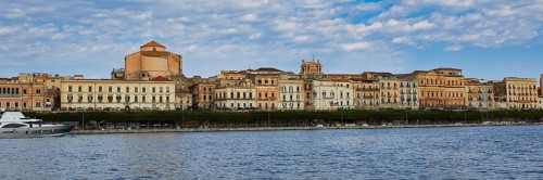 Coastal view with historic buildings against a cloudy blue sky on the promenade, boat trip around