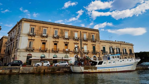 Historic coastal building with parked boat under a blue sky, boat trip around the island of
