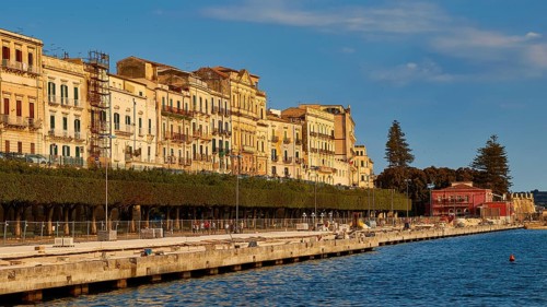 Waterfront with historic buildings and trees under a blue sky, Ortigia Island, Isola di Ortigia,