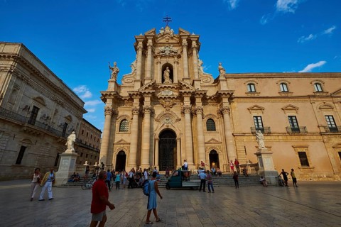 Cathedral of Syracuse, Large cathedral on a square with people and statues under a blue sky,