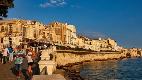 People walking along the coastal promenade with historic buildings in the evening light, Ortigia