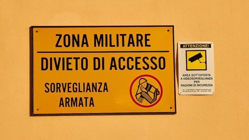 Warning sign on a wall indicating a military zone with restricted access and surveillance, Ortigia