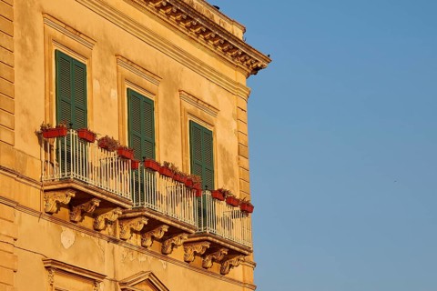 Facade of a building with balconies and green shutters in the sunlight, Ortigia Island, Isola di