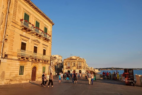 People and historic buildings on a sunny town square in the evening, Ortigia Island, Isola di
