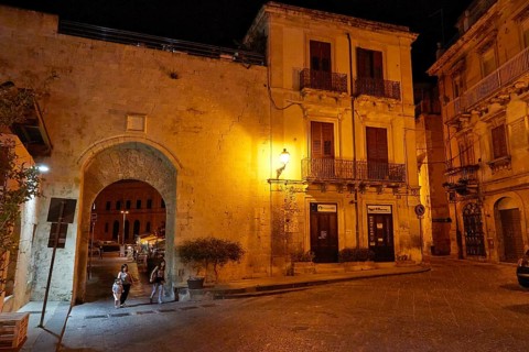 Night scene of an illuminated historic alley and a large gate with cobblestones and lantern light,