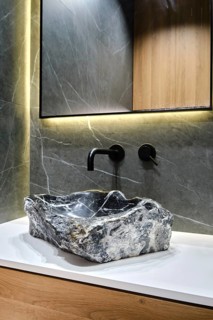 A unique stone sink made from natural rock rests on a sleek countertop in a modern bathroom. Soft