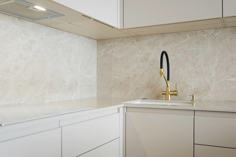 Modern minimalistic kitchen design with light stone surfaces and golden faucet