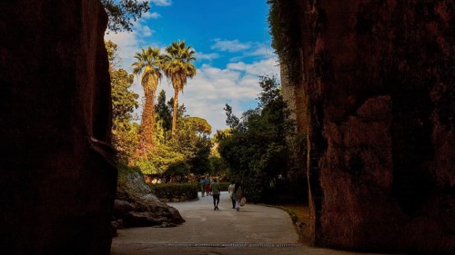 Cave Ear of Dionysus, Two people walking through a rocky passage with palm trees in the background