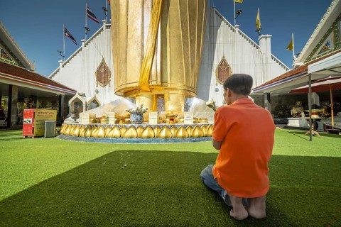 Man praying in front of a 32 metre high standing Buddha decorated with glass mosaics and 24 carat
