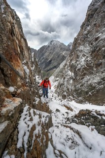 Mountaineer on a rope-secured path in a steep rocky mountain landscape with fresh snow in summer,