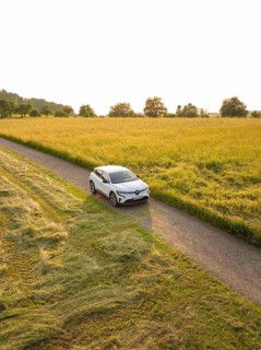 Electric car driving on a lonely country road between wide grain fields in the sunset, Renault