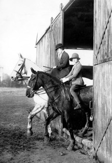 Riding horses out of a barn, 1920s, Two riders on horses coming out of a barn, wearing helmets,