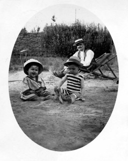 Father with 2 children beach deckchair, 1920s, Two children playing in the sand, an adult in the