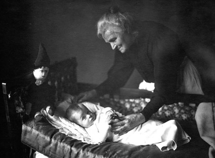 Grandma with grandson, 1930s, An elderly woman lovingly cares for a baby in a cradle, Historical