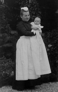 Nanny holding a baby in her arms, ca. 1910, Woman in Victorian dress holding a baby in the garden,