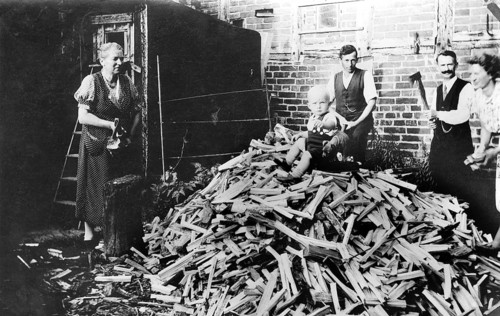 Baby sitting on a mountain of firewood, 1930s, family working together in the yard chopping wood