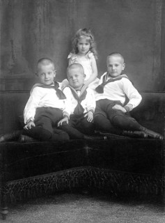 Three boys and a girl, 1930s, Three boys and a girl in traditional dress pose together on a sofa,