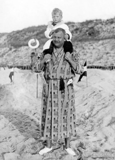Man in bathrobe carrying child on shoulders, 1930s, A father carries his child on his shoulders on