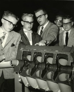 Pupil looks bored while teacher explains, 1950s, group of men examining a technical model. All