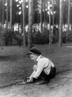 Child cutting grass, 1920s, A boy concentrates on playing with a shovel in the forest floor,