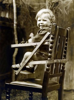 Baby in a child seat, 1930s, A smiling toddler sits happily in a wooden high chair, outside in a