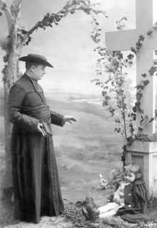 Man blessing a child, 1930s, A priest talks to a child next to a large cross, Historical photo