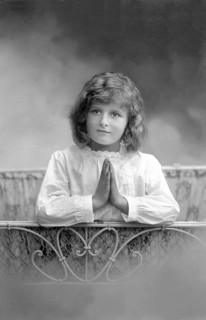 Girl praying at bedside, 1930s, A girl prays with folded hands in front of a bed, Historical photo