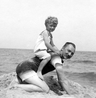 Son sitting on his father on the beach, 1920s, A man on his hands and knees with a happy child on