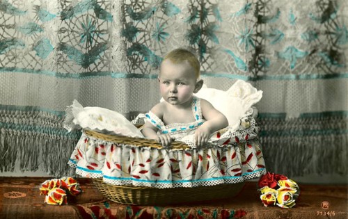 Baby sitting in basket, 1905, A baby sits in a decorative basket draped with colourful fabric,